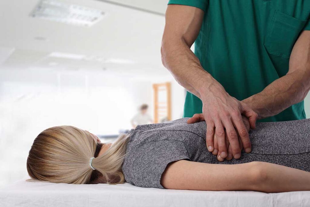 A person at home uses a heating pad on their lower back while sitting on a couch.