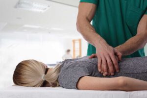 A person at home uses a heating pad on their lower back while sitting on a couch.