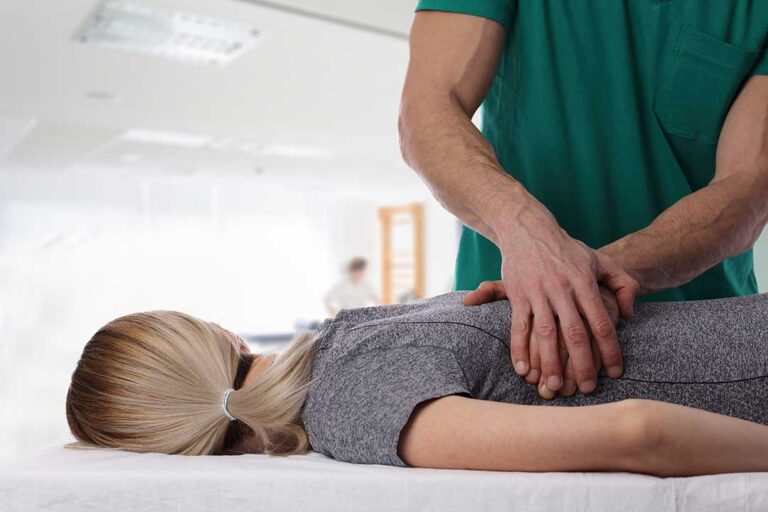A person at home uses a heating pad on their lower back while sitting on a couch.